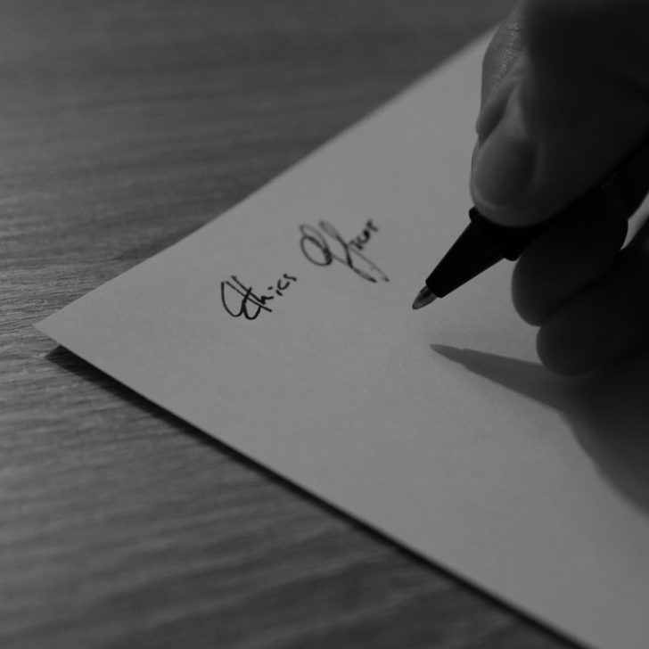 Hand schreibt mit einem Stift eine Beschreibung auf ein Blatt Papier.