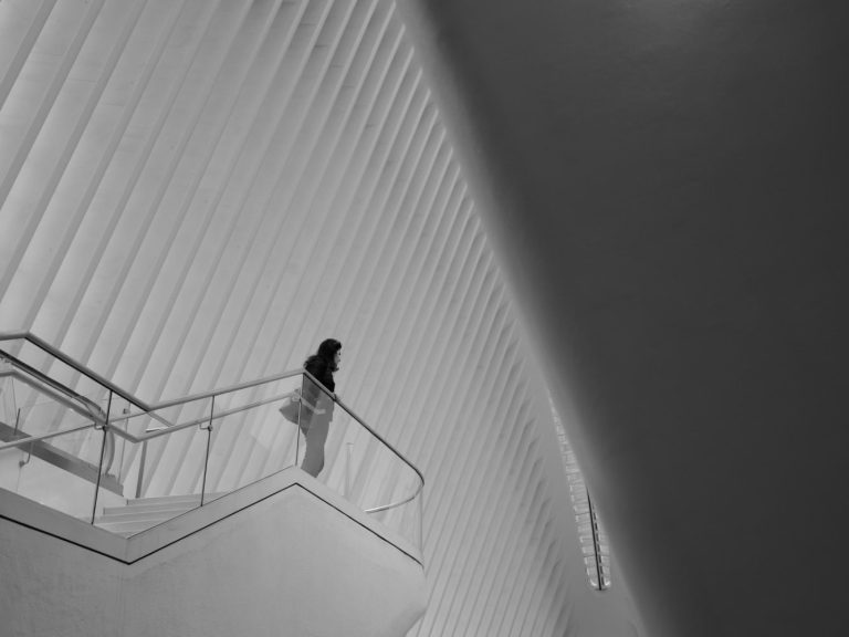 Person geht eine Treppe in einem modernen, hellen Gebäude mit geometrischen Linien hinauf.