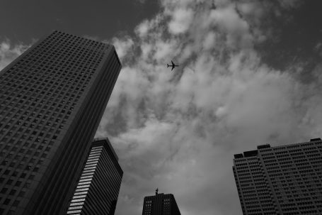 Hochhäuser unter bewölktem Himmel mit einem Flugzeug, das darüber fliegt.