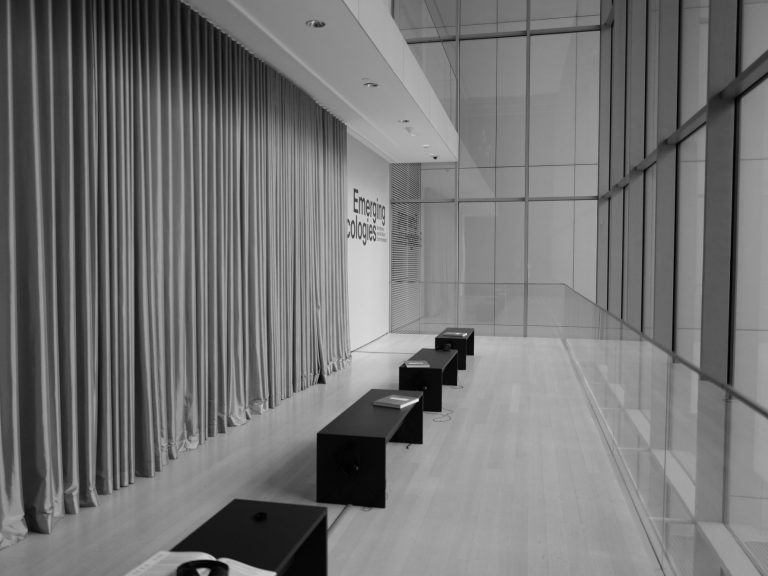 Innenraum mit Holzfußboden, langen Vorhängen und mehreren schwarzen Bänken.