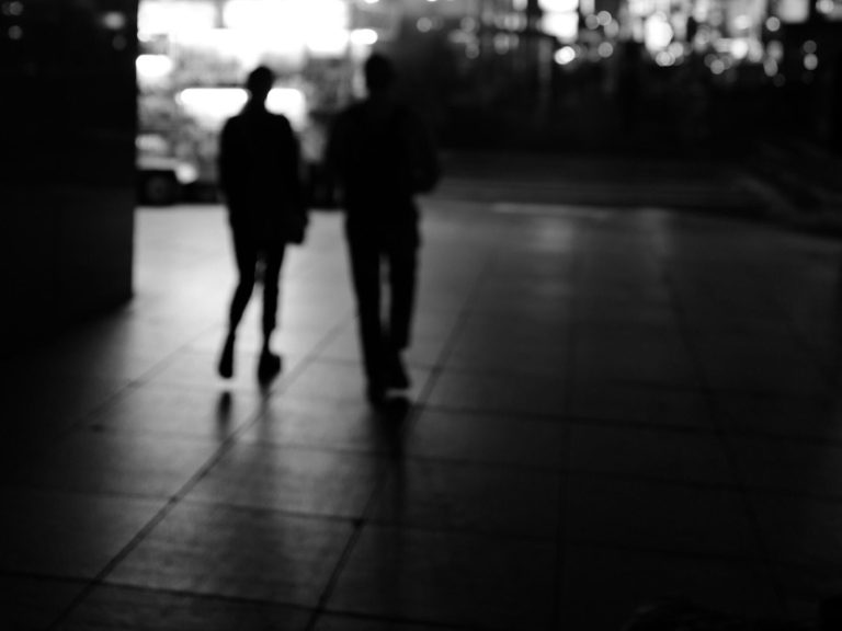 Silhouetten zweier Personen, die auf einem Gehweg in der Dämmerung gehen.
